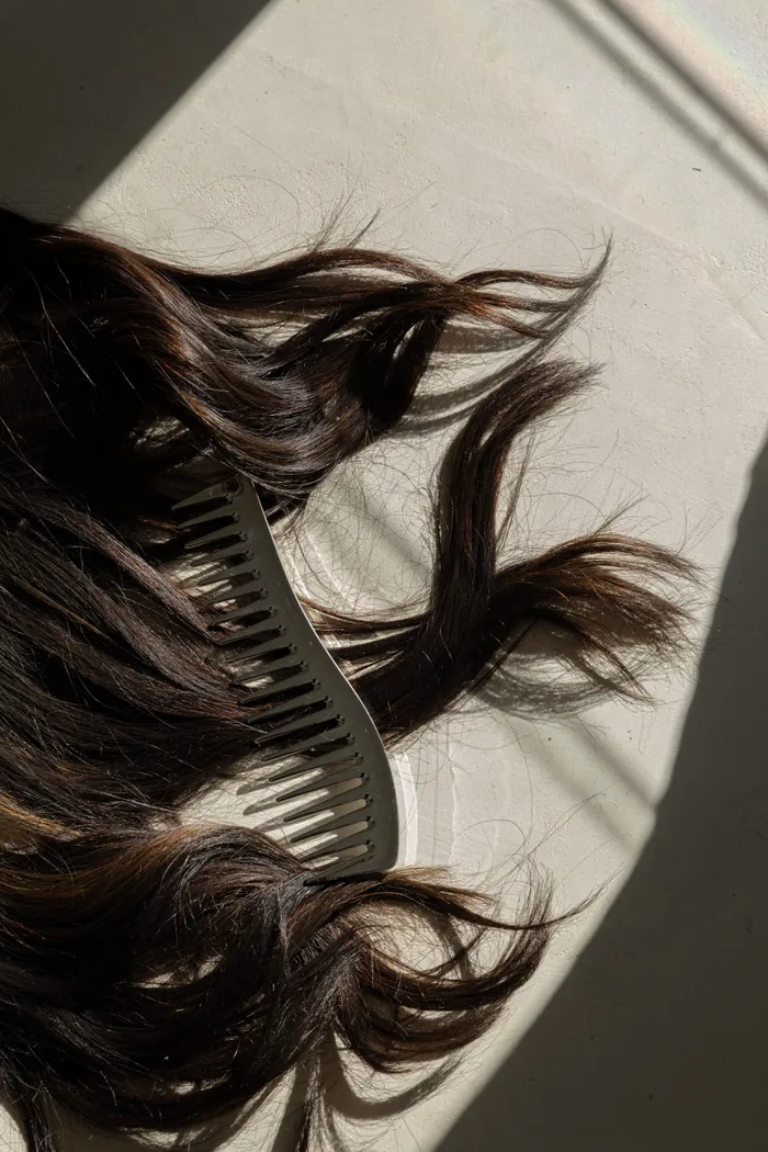 Dark hair with comb on white surface in natural light