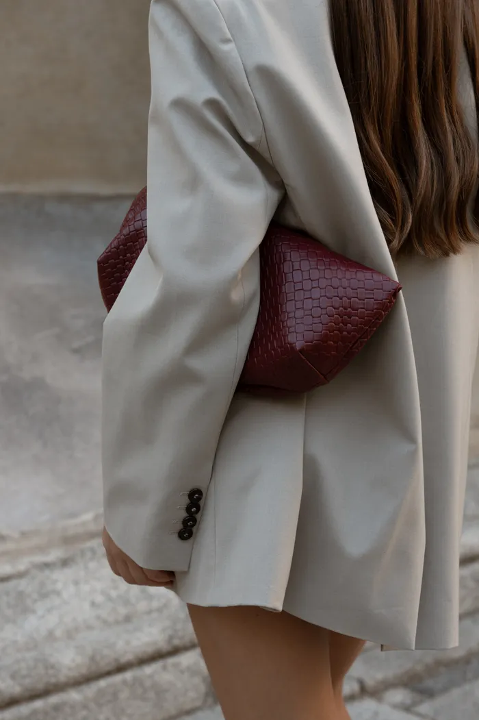 Woman in a cream blazer carrying a burgundy woven handbag